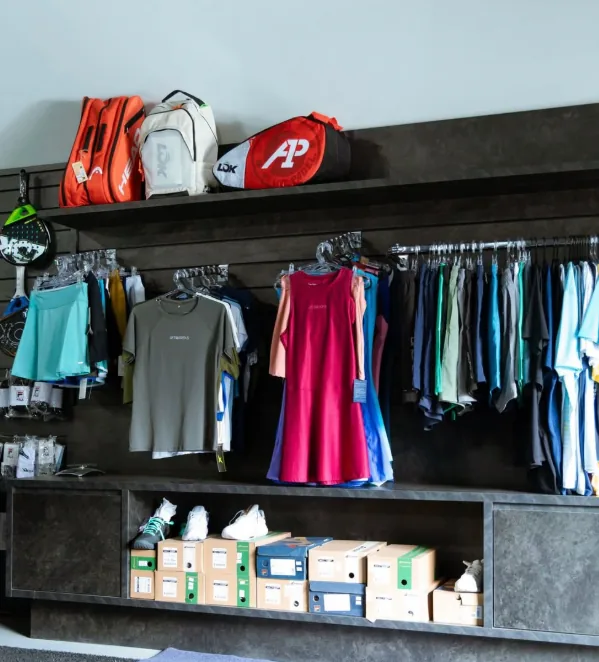 Interior da West Padel Store: raqueteiras na prateleira, roupas de padel nas araras e caixas de tênis embaixo.