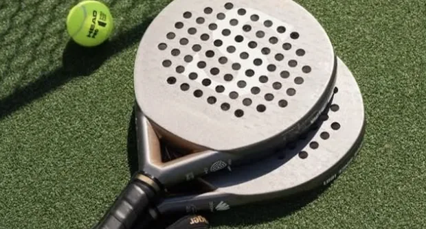 Duas raquetes de padel e bolas sobre a grama sintética, ao lado da rede.